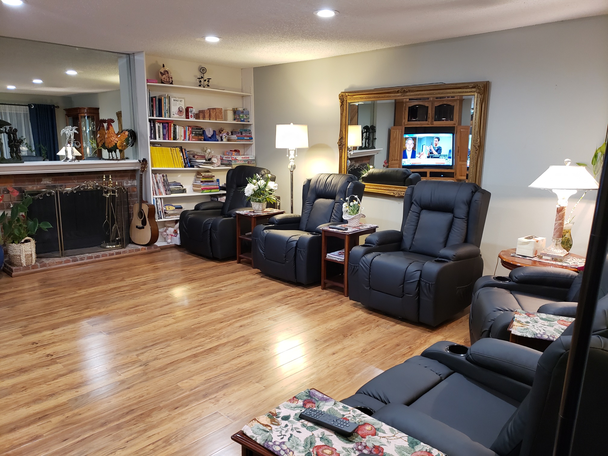 A simple bedroom in one of the Snohomish County adult family homes, featuring a hospital bed with a blue quilt, a white recliner, nightstand with lamp, and wall art of a forest waterfall.